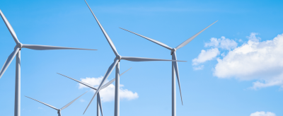 A row of wind turbines against a clear blue sky with scattered clouds.