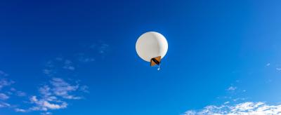 A white balloon floats in a clear blue sky with scattered clouds.