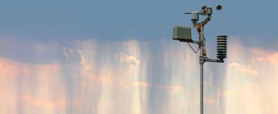 A weather station with instruments stands against a backdrop of a sky with wispy, falling streaks of rain or cloud.