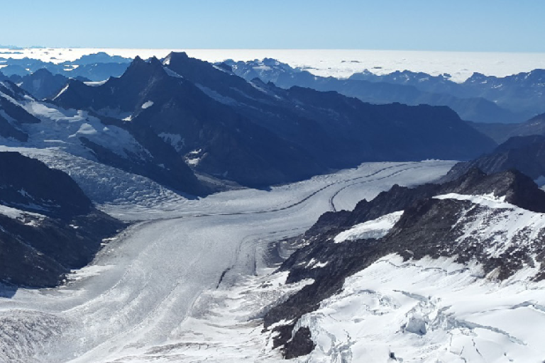 View of a glacier surrounded by snow-covered mountains, with blue sky in the background. Text overlay: "Glaciers Essential Climate Variable (ECV) Factsheet" and associated logos.