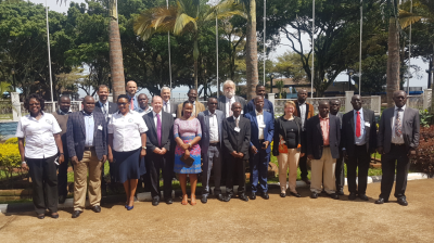 Group of people standing outdoors in front of palm trees, dressed in formal and casual attire.
