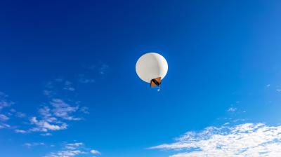 A white balloon floats in a clear blue sky with scattered clouds.