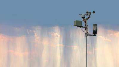A weather station with instruments stands against a backdrop of a sky with wispy, falling streaks of rain or cloud.