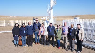 A group of people standing together outside near a spiral staircase and a white fence in a field under a clear blue sky.