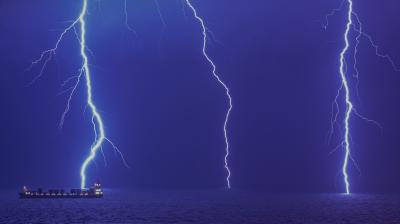 A ship sails on the ocean at night as two bright lightning bolts strike the water.