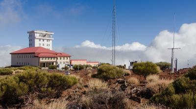 A research observatory building with a red roof, surrounded by dry shrubs and antennas, under a blue sky with scattered clouds.