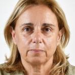 A person with shoulder-length blonde hair and a neutral expression is facing the camera against a plain background.