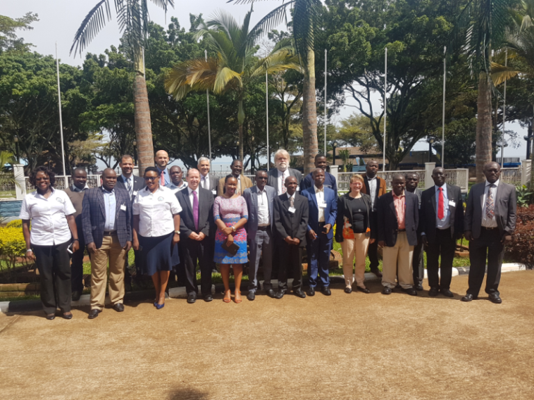 Group of people standing outdoors in front of palm trees, dressed in formal and casual attire.